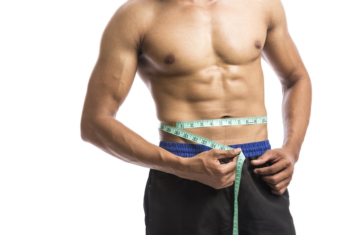 Fit man measuring his waist with tape measure, isolated on white background