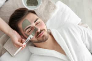 Cosmetologist applying mask on a man's face in spa salon