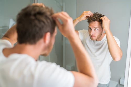 Hair loss man looking in bathroom mirror