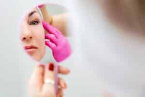 Woman looking in the mirror as doctor evaluates her facelift recovery and results