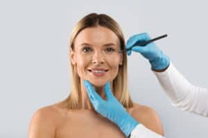 Mature woman with doctor's hands about to mark her face for facelift in Salt Lake City